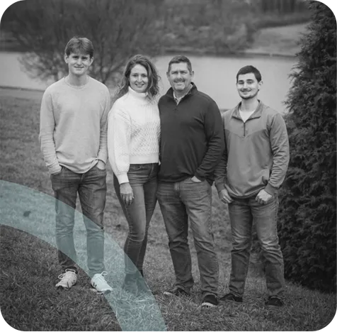 Josh Honaker with his family, on a lawn by a pond, in black and white.