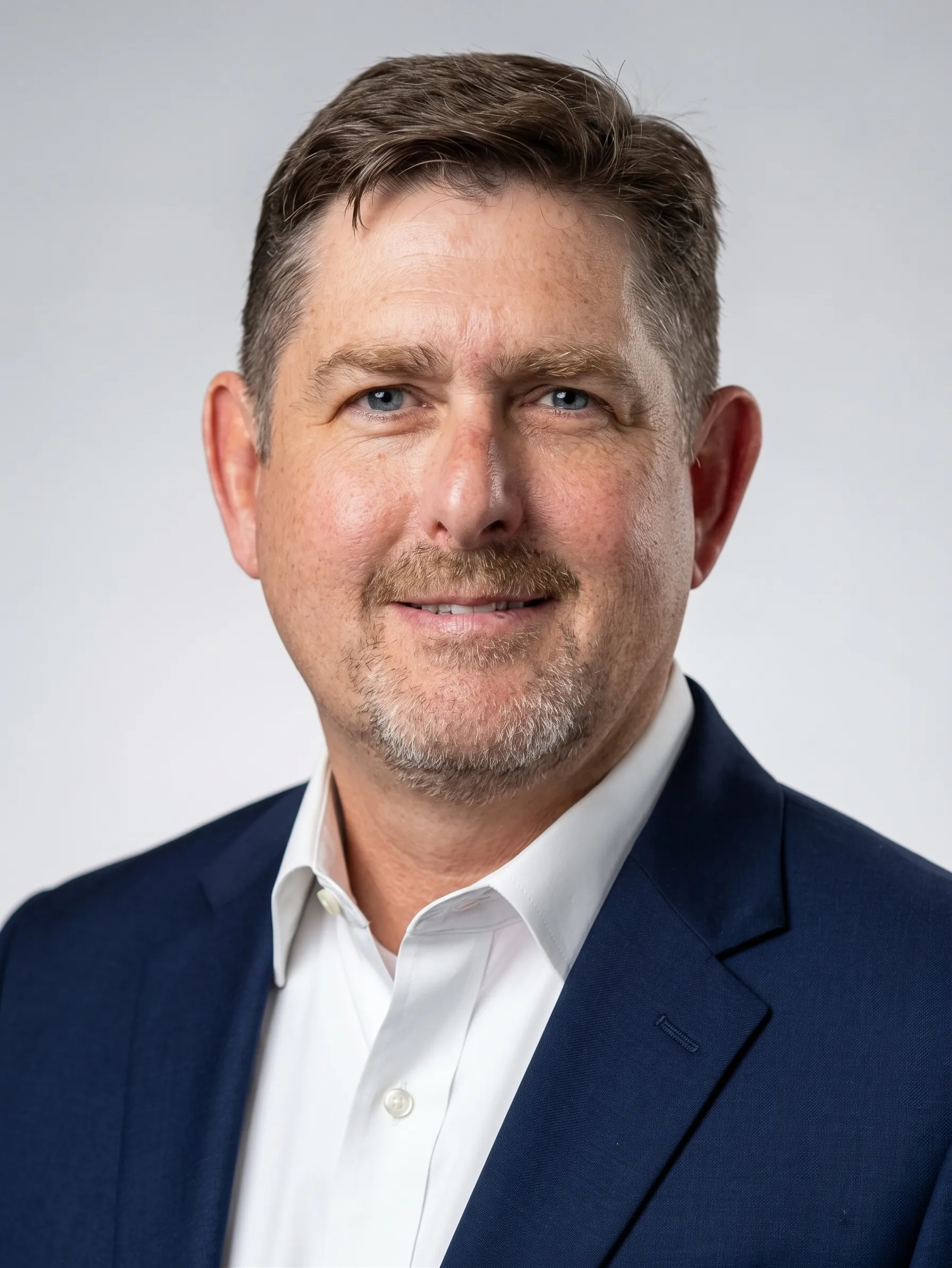Dr. Josh Honaker in a navy blazer and white shirt, smiling, against a light gray background.
